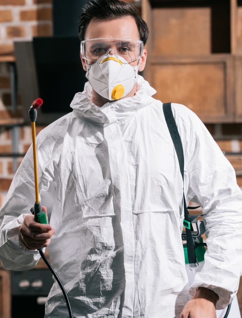 Person in protective suit holding sprayer.